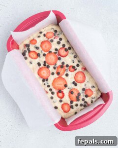 batter added in a baking pan and topped with sliced strawberries and chocolate chips.