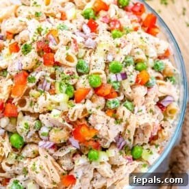 A top-down shot of a clear glass bowl showcasing creamy tuna macaroni salad, generously mixed with vibrant ingredients.