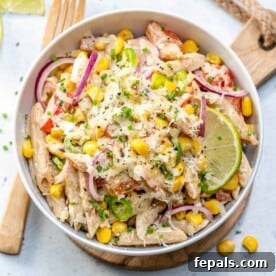 A Mexican-style pasta salad, beautifully arranged in a round bowl and garnished with shredded cheese and fresh lime wedges, highlighting its vibrant ingredients.