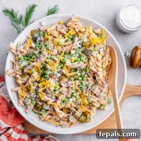 A wooden spoon gently stirs a large white bowl of creamy dill pickle pasta salad, highlighting its rich, well-mixed texture and inviting appearance.