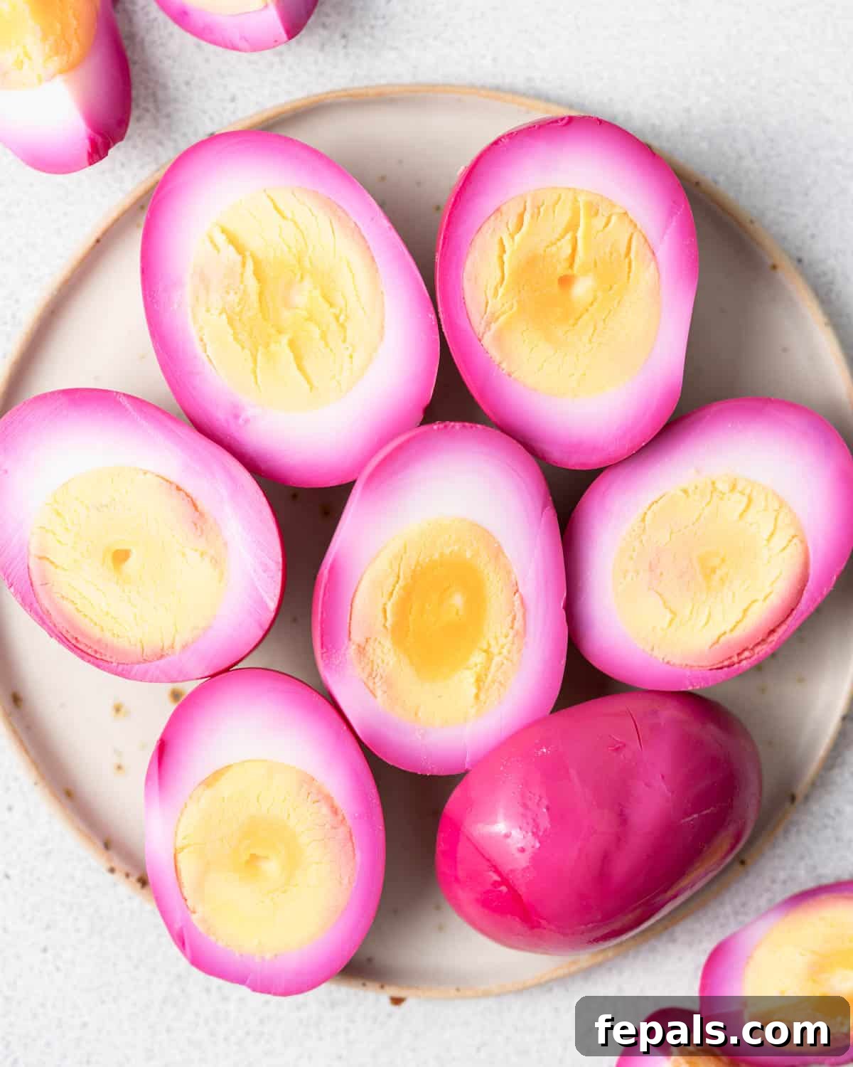 Ruby Red Pickled Eggs 2 Halved pink pickled eggs arranged on a white plate with sliced beets, showing bright magenta-stained whites and golden-yellow yolks, ready to serve.