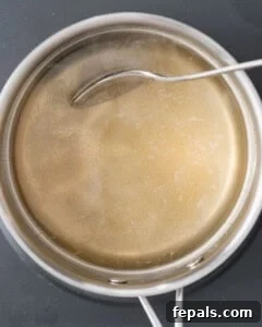 Ruby Red Pickled Eggs 13 Large stainless steel pot containing warm golden-brown pickling brine being stirred with a white spoon.