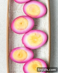 Ruby Red Pickled Eggs 15 Multiple halved pink pickled eggs laid out in a row on a rectangular tray lined with textured cloth or parchment.