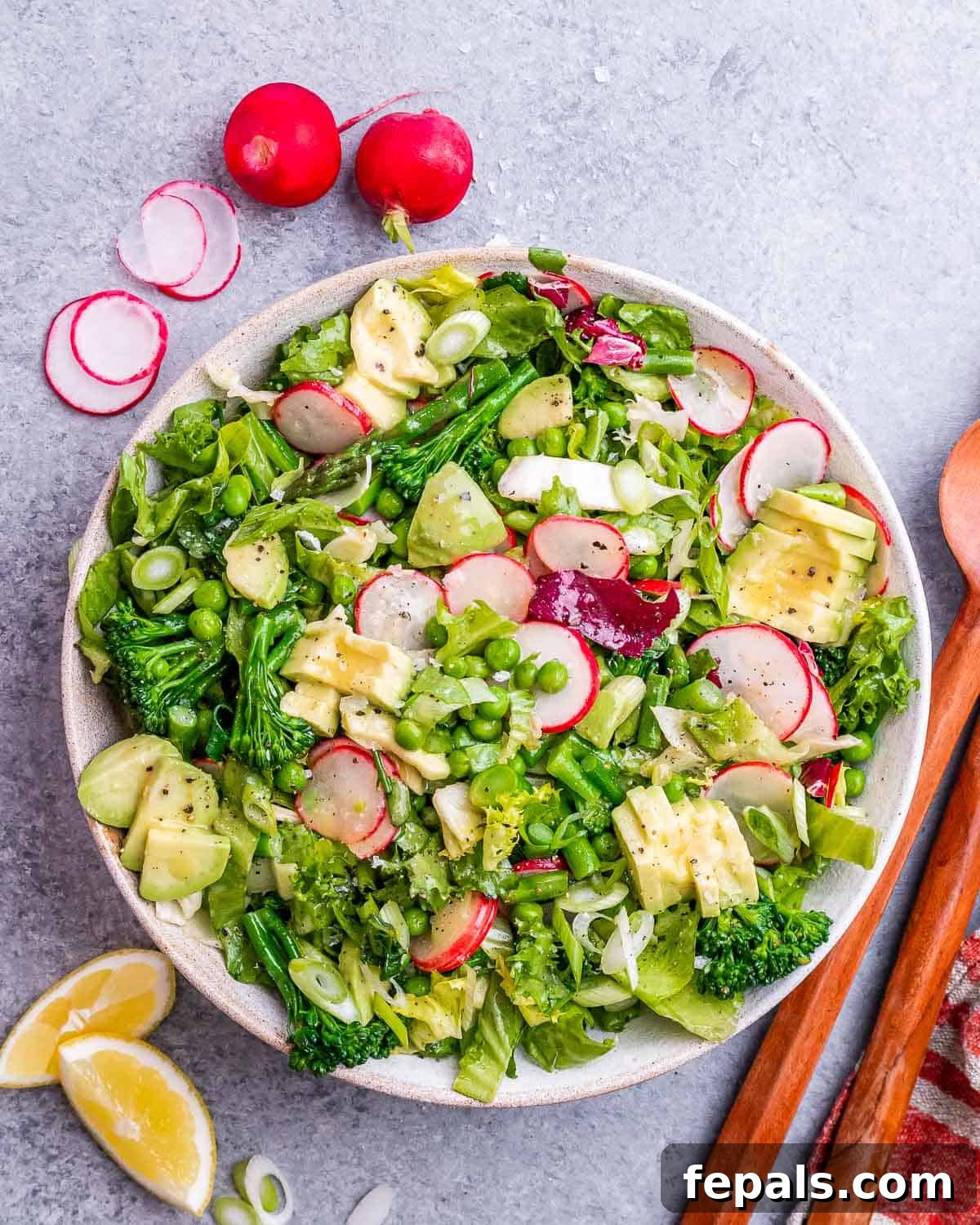 A vibrant bowl of spring mix salad, generously topped with thinly sliced radishes, tender broccoli florets, fresh asparagus spears, and bright green peas, showcasing a healthy and appealing meal.
