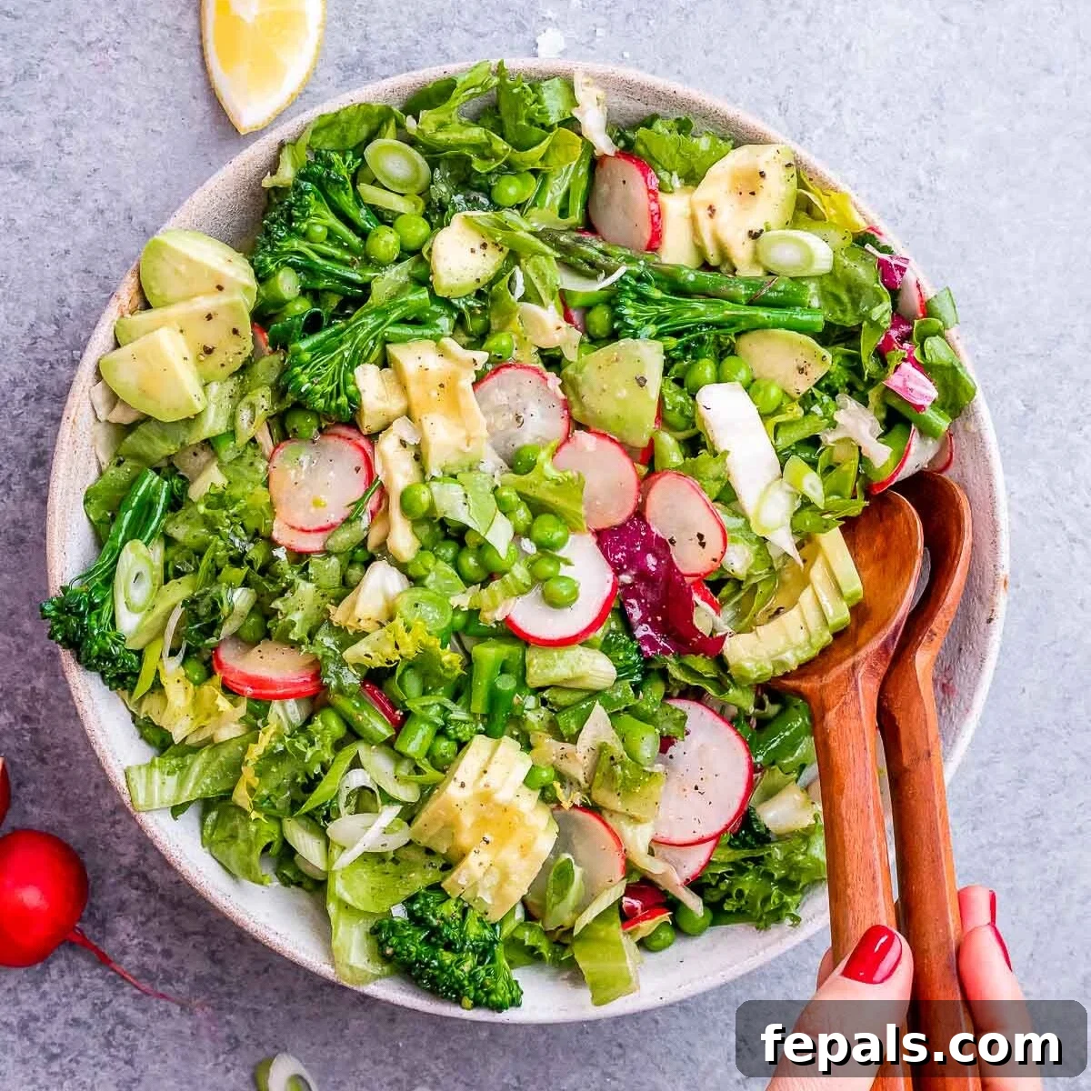 Close-up shot of salad tongs reaching into a vibrant bowl of spring mix salad, ready to be served.