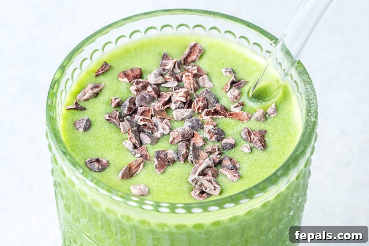 A refreshing green shamrock protein smoothie in a glass with a straw, garnished with cocoa nibs.