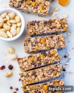 Rectangle Healthy Granola Bars in a line on a light surface next to a bowl of nuts.