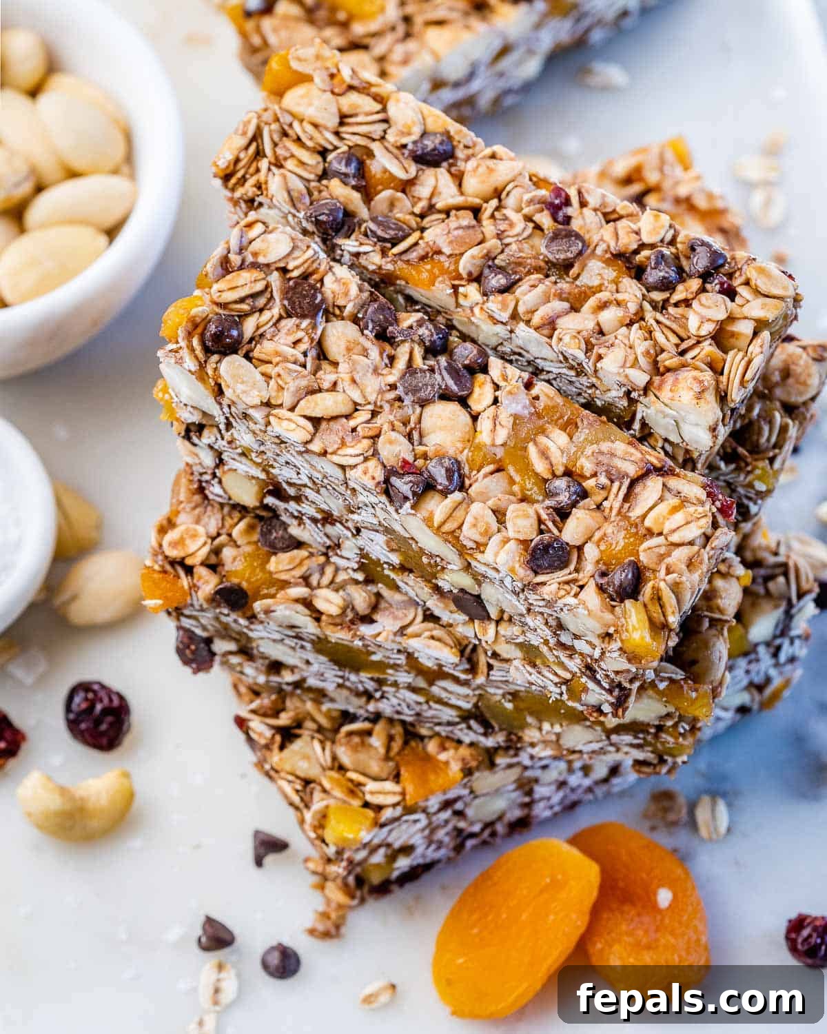 Stack of cut healthy granola bars arranged on a white surface, displaying golden toasted edges, oats, nuts, apricots, cranberries, and dark chocolate chips.