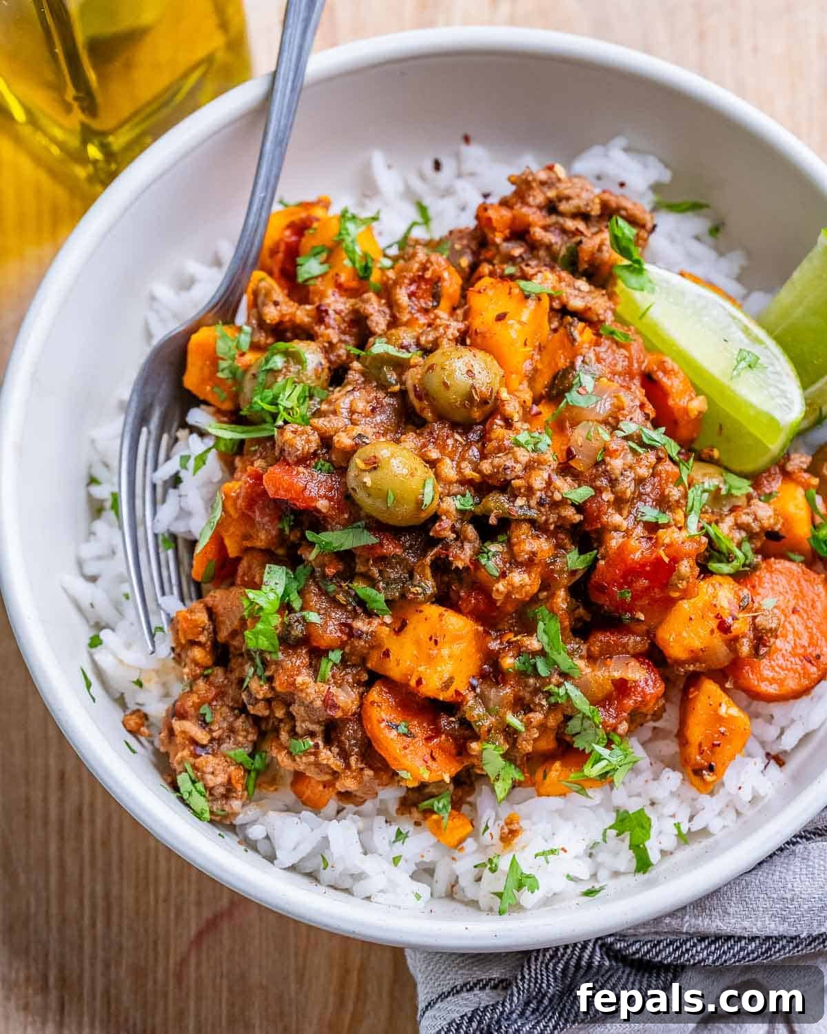 Hearty Mexican Picadillo 2 A white bowl of rice with Mexican picadillo and lime wedges, showcasing a hearty and vibrant meal.