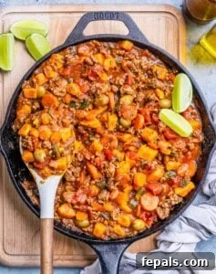 A black skillet of Mexican picadillo on a wooden board.