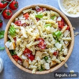 Chicken Caesar pasta salad in a round brown bowl with lettuce, pasta, grilled chicken, and tomatoes.