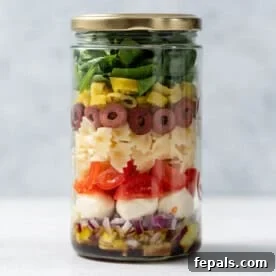 Vibrant Italian pasta salad layered beautifully in a clear glass jar, showing colorful vegetables and pasta.