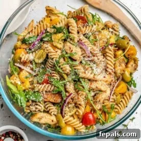 A large bowl of colorful chicken pasta salad, mixed with chicken and a variety of fresh vegetables.