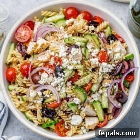 Top view of a vibrant Greek chicken pasta salad in a white bowl, featuring pasta, chicken, and Mediterranean ingredients.