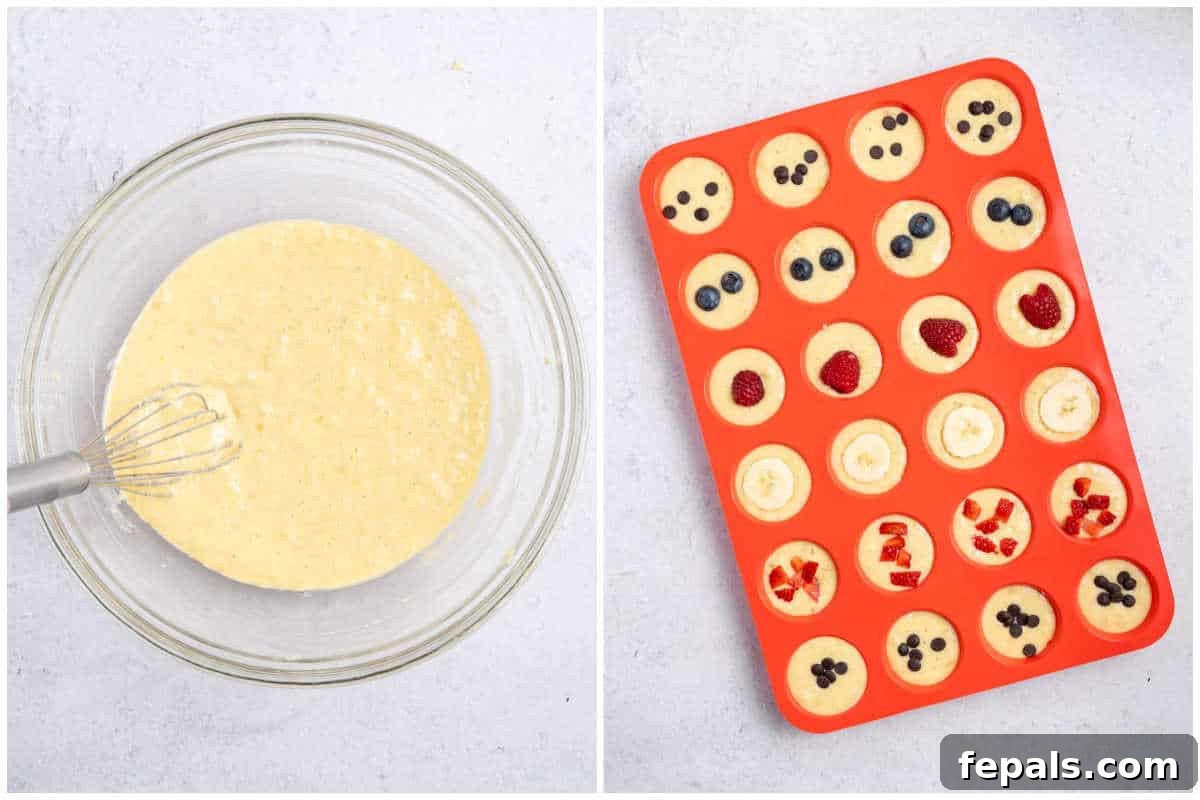 Process shot showing mini muffin silicone molds filled with pancake batter and topped with colorful fruits, ready for baking.