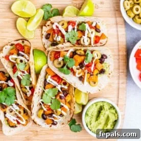 Four hearty black bean and sweet potato tacos arranged on a rustic cutting board, highlighting a wholesome vegetarian option.