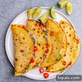 A close-up of four perfectly folded shredded chicken tacos, elegantly garnished with vibrant cherry tomatoes, spicy jalapeños, and refreshing lime wedges.