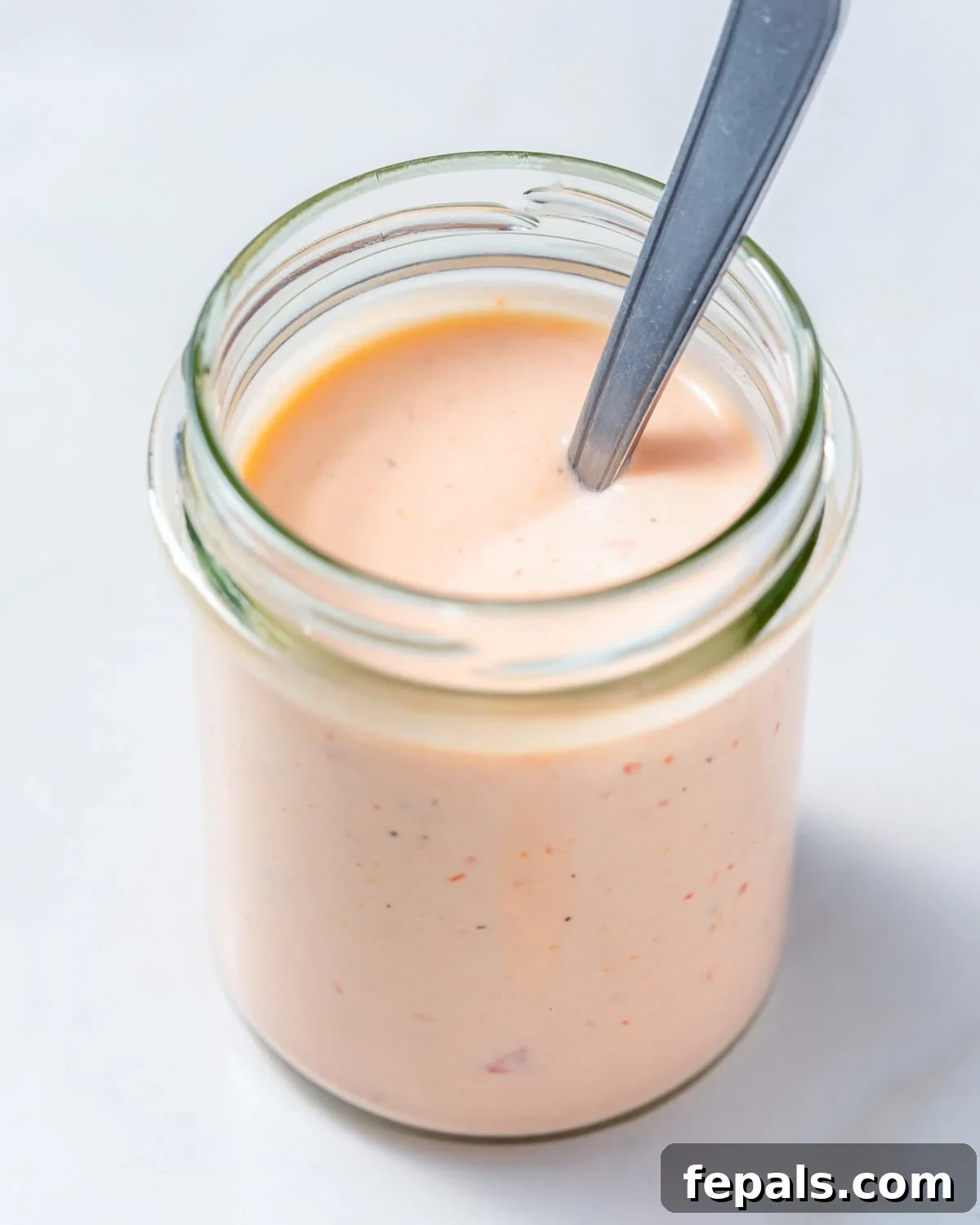 Irresistible Bang Bang Sauce 2 A jar with homemade Bang Bang Sauce, featuring a spoon dipped inside, ready to serve.