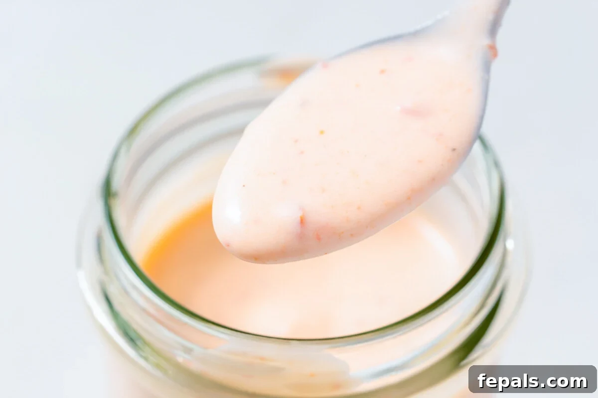 Irresistible Bang Bang Sauce 7 A spoonful of creamy Bang Bang sauce gracefully dripping from a spoon back into a jar.