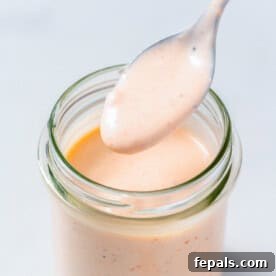 A jar filled with Bang Bang sauce, featuring a spoonful of the sauce above it.