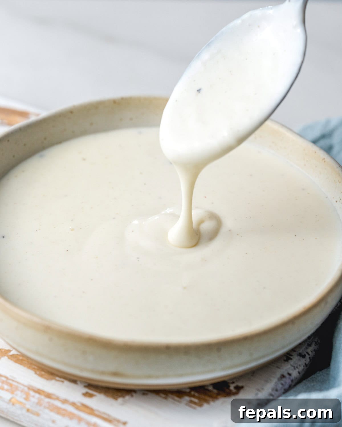 A bowl with perfectly smooth Bechamel sauce, with a spoon gently dipped into its creamy depths, hinting at its luxurious texture.