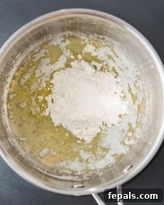 Flour being vigorously whisked into melted butter in a pan, forming a smooth roux for Bechamel sauce.
