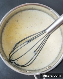 A whisked Bechamel sauce simmering in a pan, thickening to its desired creamy consistency.