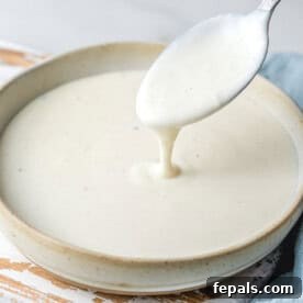 A bowl with bechamel sauce and a spoon dipped in the sauce.