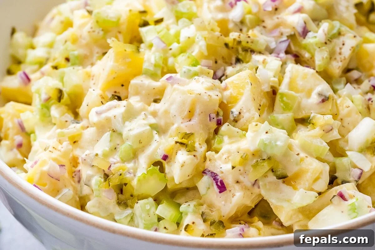 Bowl of potato salad before final mixing, highlighting colorful layers of ingredients like red onion and celery.