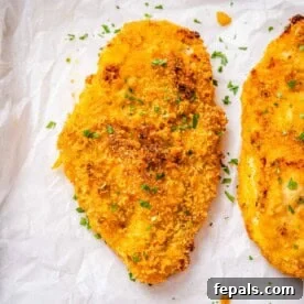 Crispy baked chicken breast on a sheet pan topped with chopped parsley.