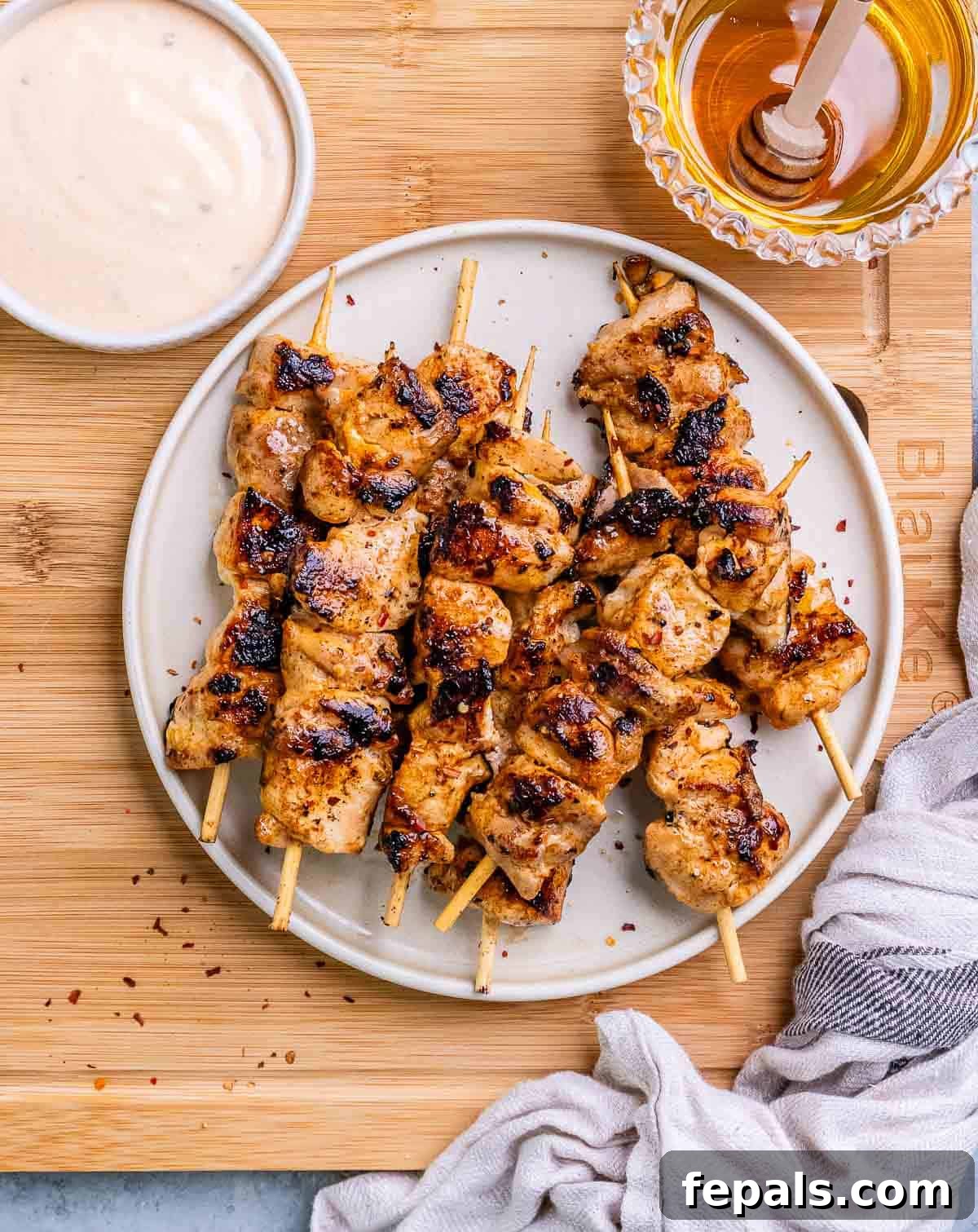 Firecracker Chicken Skewers 7 A beautiful presentation of grilled bang bang chicken skewers on a white plate set on a wooden board.