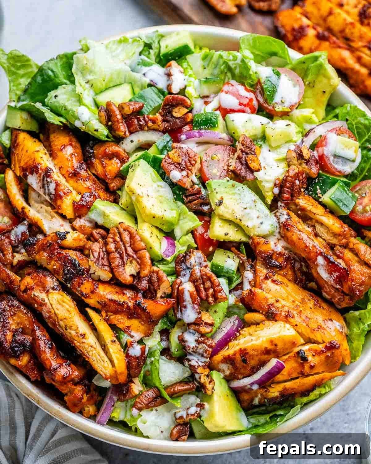 a salad bowl topped with grilled bbq chicken and drizzled with a homemade dressing.