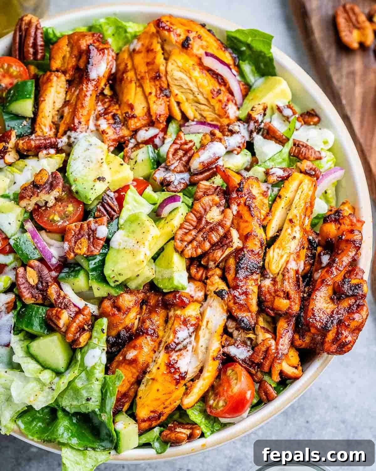 a bowl filled with salad topped with sliced bbq chicken thighs and other veggies.