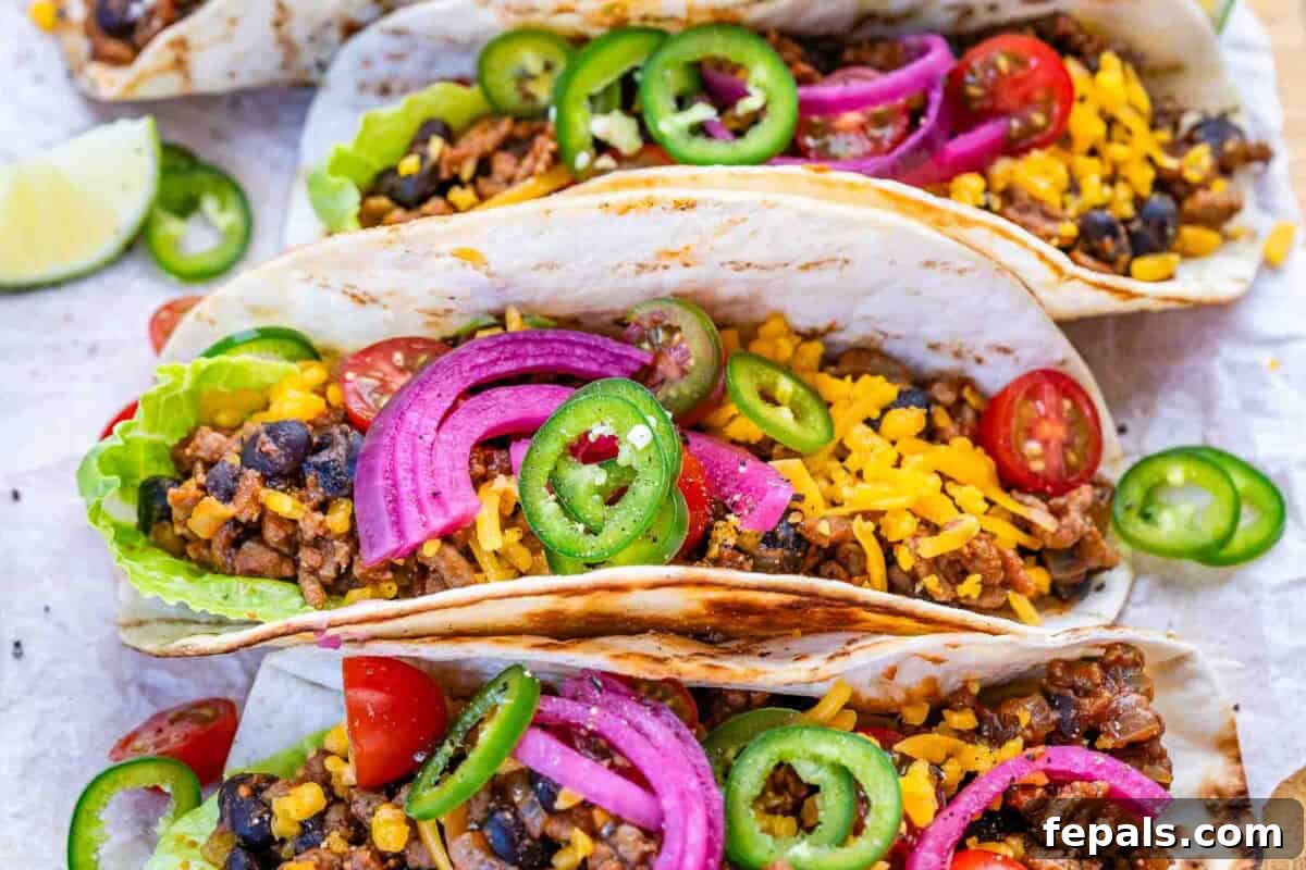 ground beef tacos assembled and topped with pickled onions and sliced jalapenos.