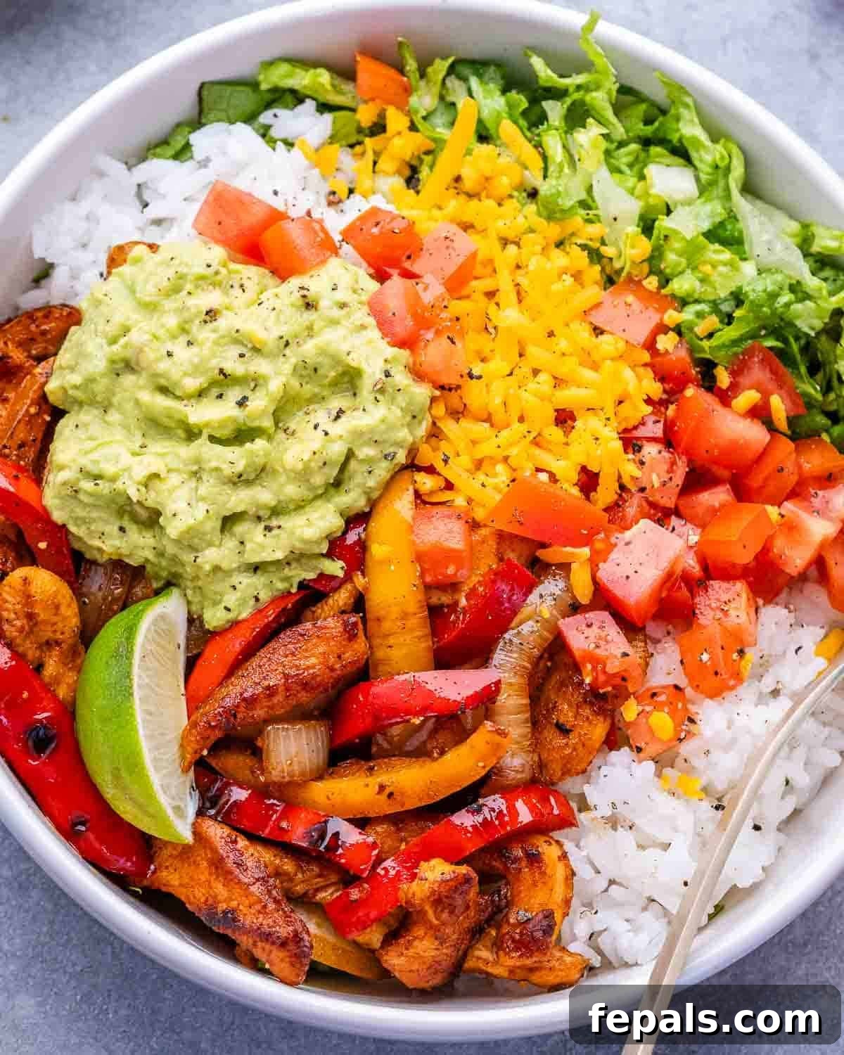 Chicken Fajita Rice Bowl with Peppers & Onions 2 A closeup of a white bowl with chicken, peppers, onions, lettuce, rice and cheese.