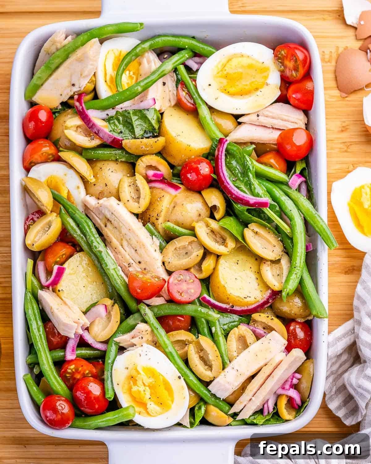 Nicoise salad with eggs, potatoes, olives, green beans and tuna in a white serving dish.
