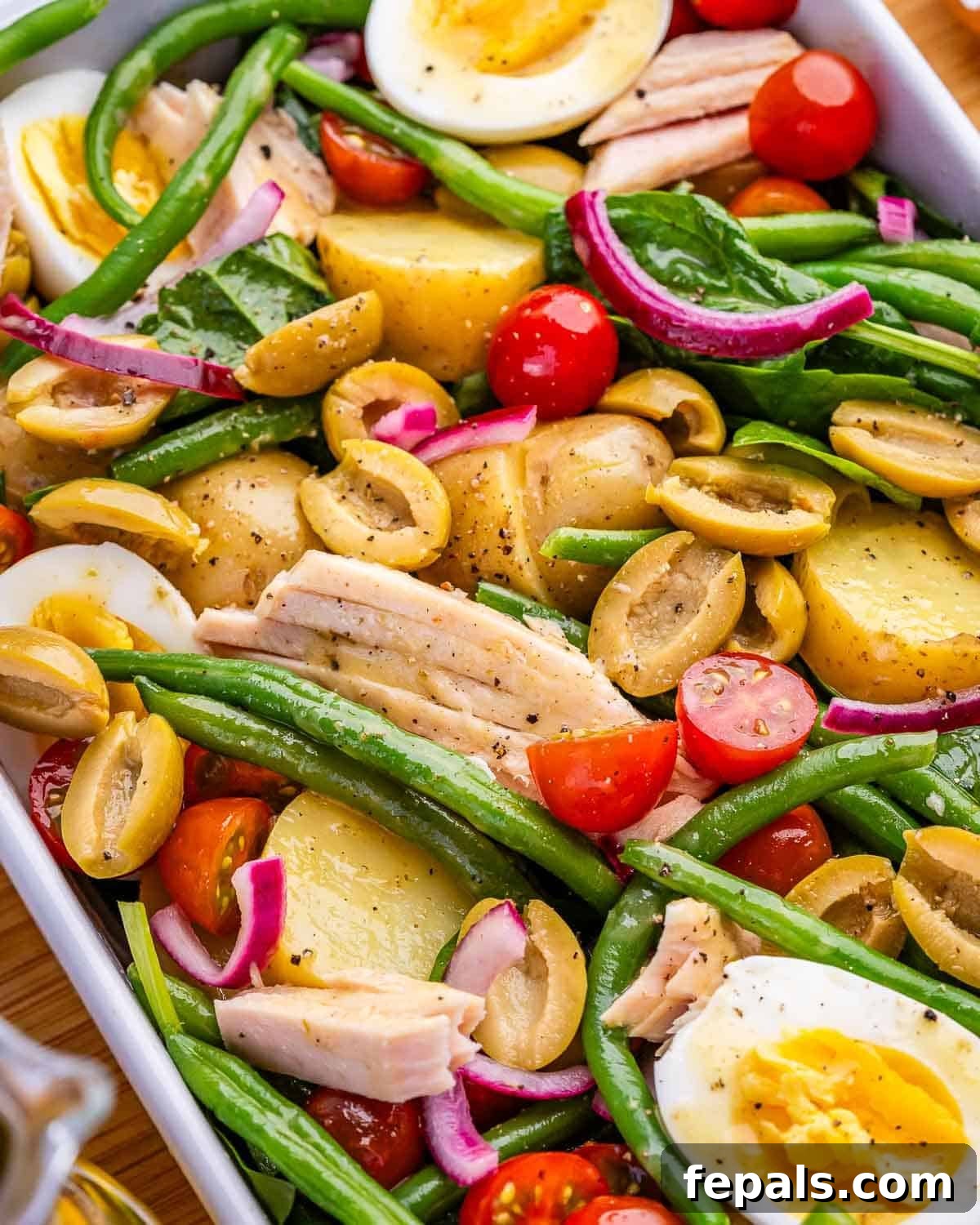 A close up image of Nicoise salad with olives, tuna, potatoes, eggs, green beans and tomatoes.