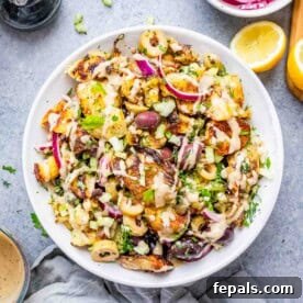 A vibrant bowl of smashed potato salad with a creamy tahini dressing, olives, and fresh herbs.