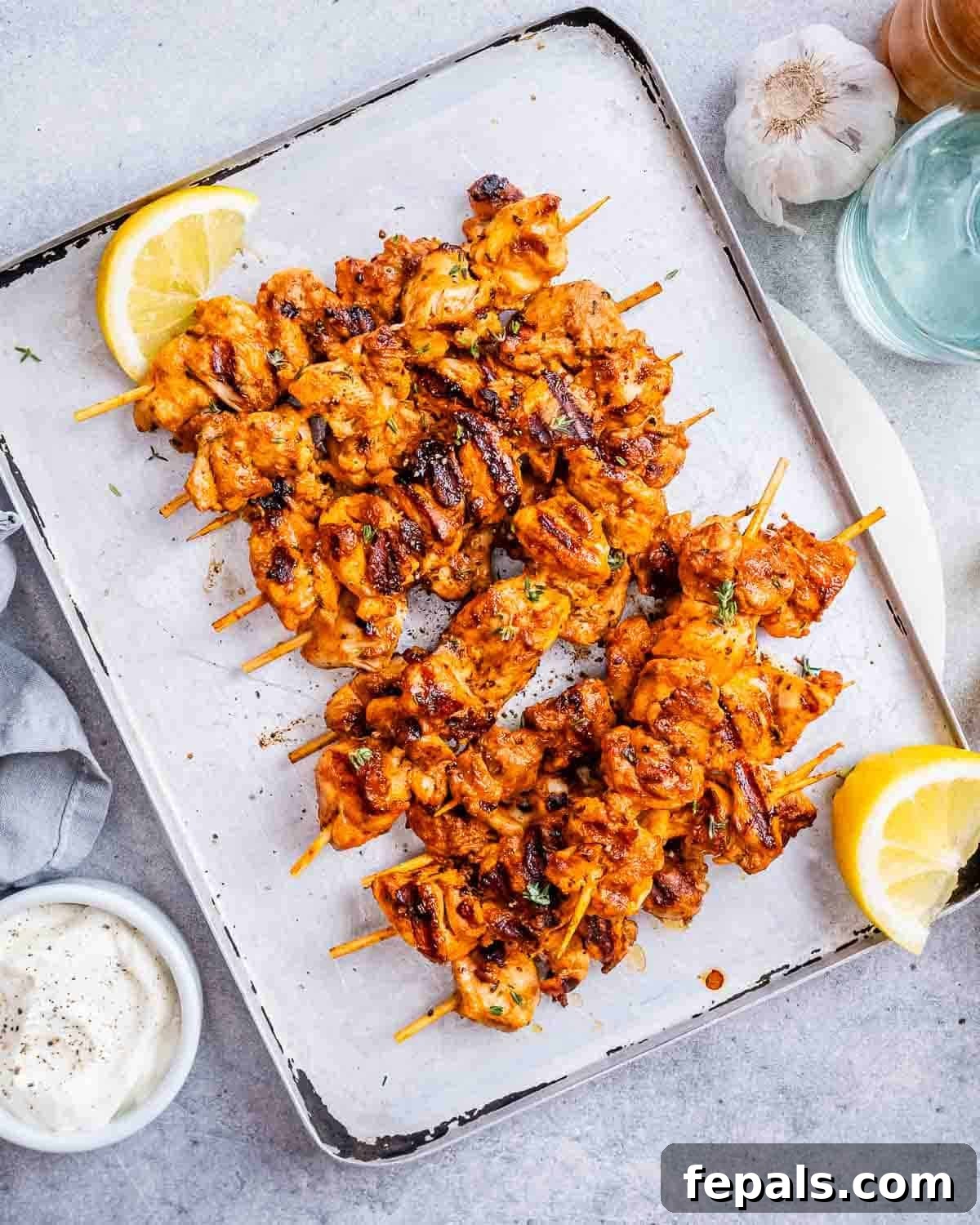 Yogurt marinated chicken on a sheet pan with lemon wedges.