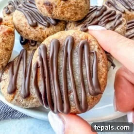A hand holding a perfectly formed date cookie with a chocolate drizzle, showcasing its texture.