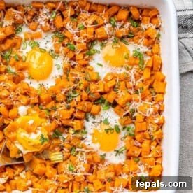 A sheet pan sweet potato breakfast hash with perfectly cooked eggs nestled among the vegetables.