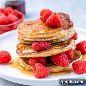 Stacks of light and fluffy cottage cheese pancakes garnished with fresh raspberries and drizzled with maple syrup.