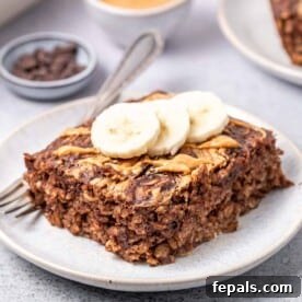 A slice of peanut butter brownie baked oatmeal on a plate, topped with banana slices for a decadent breakfast.