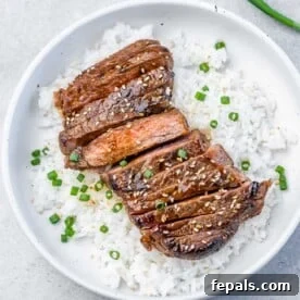 15-Minute Beef Dinners for Busy Weeknights 12 A round white plate with white rice topped with sliced teriyaki steak garnished with chopped green onions and sesame seeds.