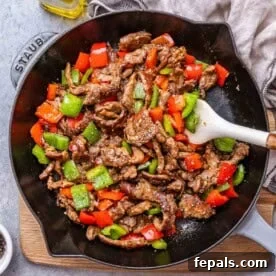 15-Minute Beef Dinners for Busy Weeknights 20 a skillet with black pepper beef made with green and red bell peppers, but white spoon in the skillet.