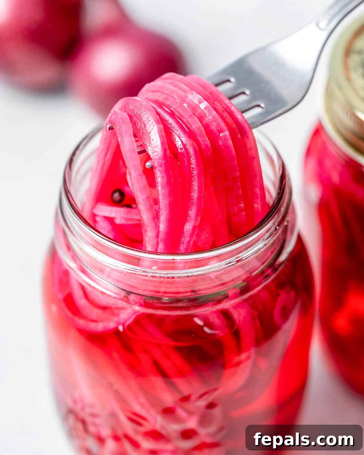 Quick Pickled Red Onions You’ll Prefer Over Store-Bought 2 pickled red onions in a jar with fork grabbing some from the jar.