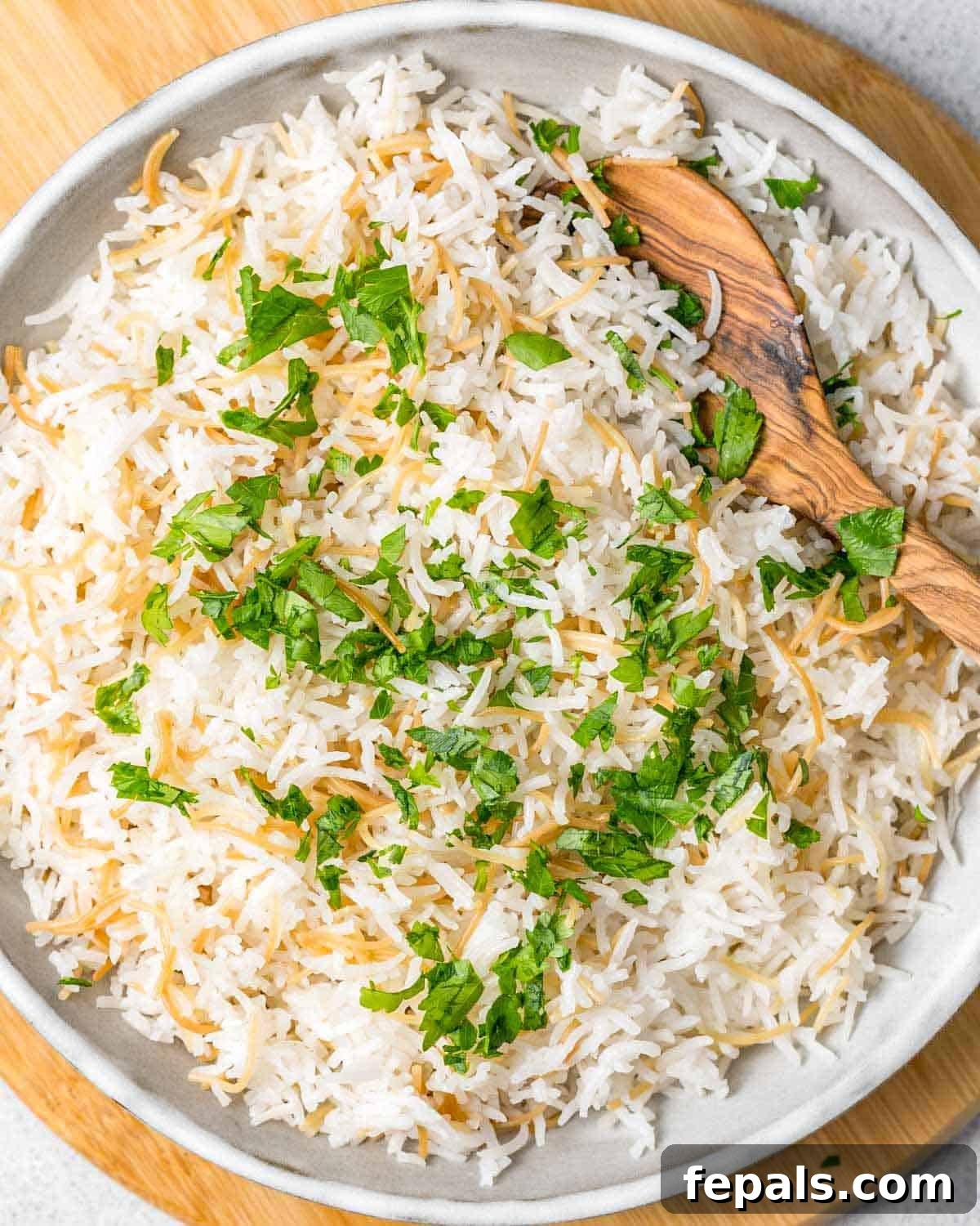 Classic Lebanese Vermicelli Rice 2 A large ceramic bowl filled with fluffy Lebanese rice and vermicelli, with a wooden spoon resting inside.