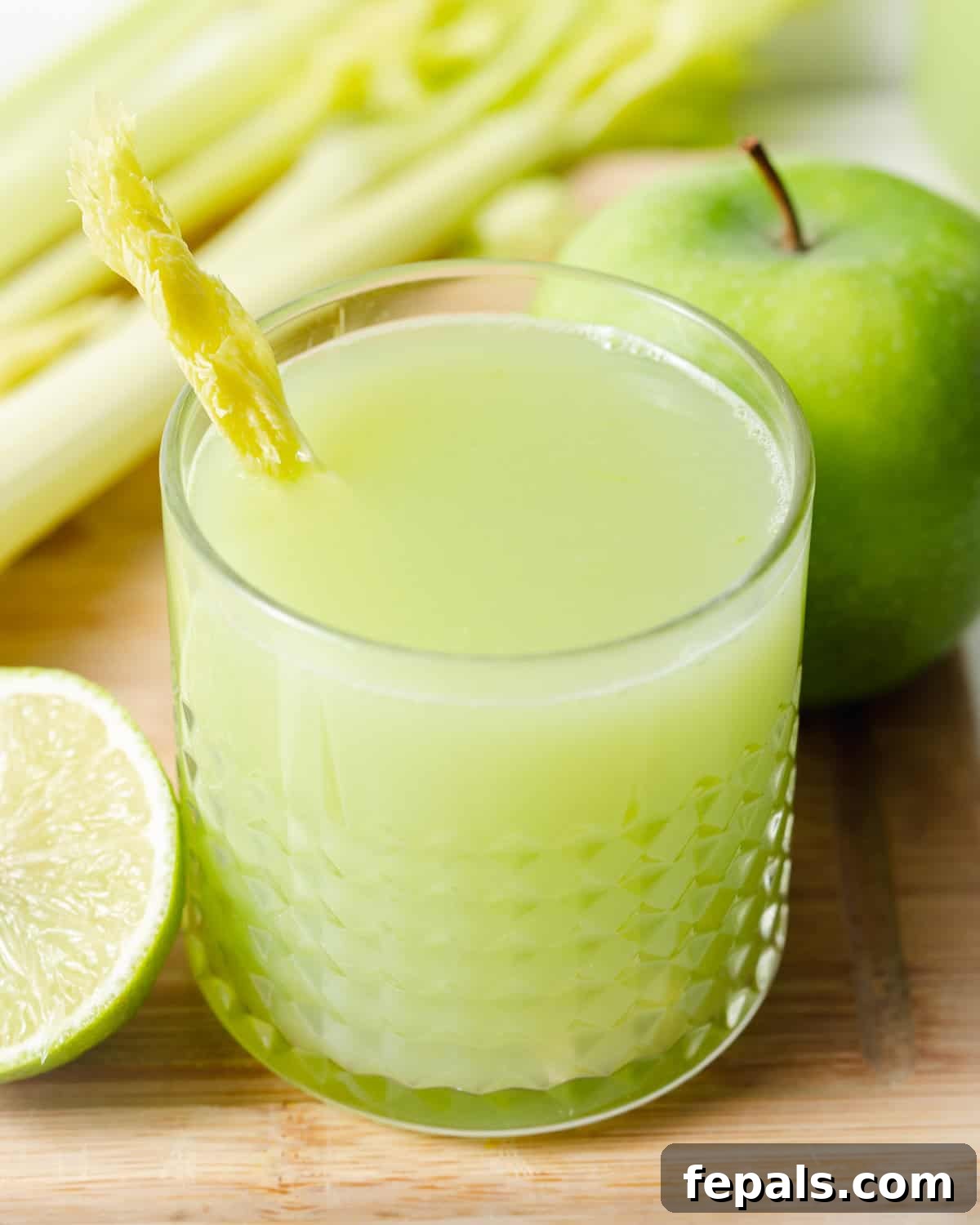 A tall glass of vibrant green celery juice garnished with a lime wedge and celery stalk.
