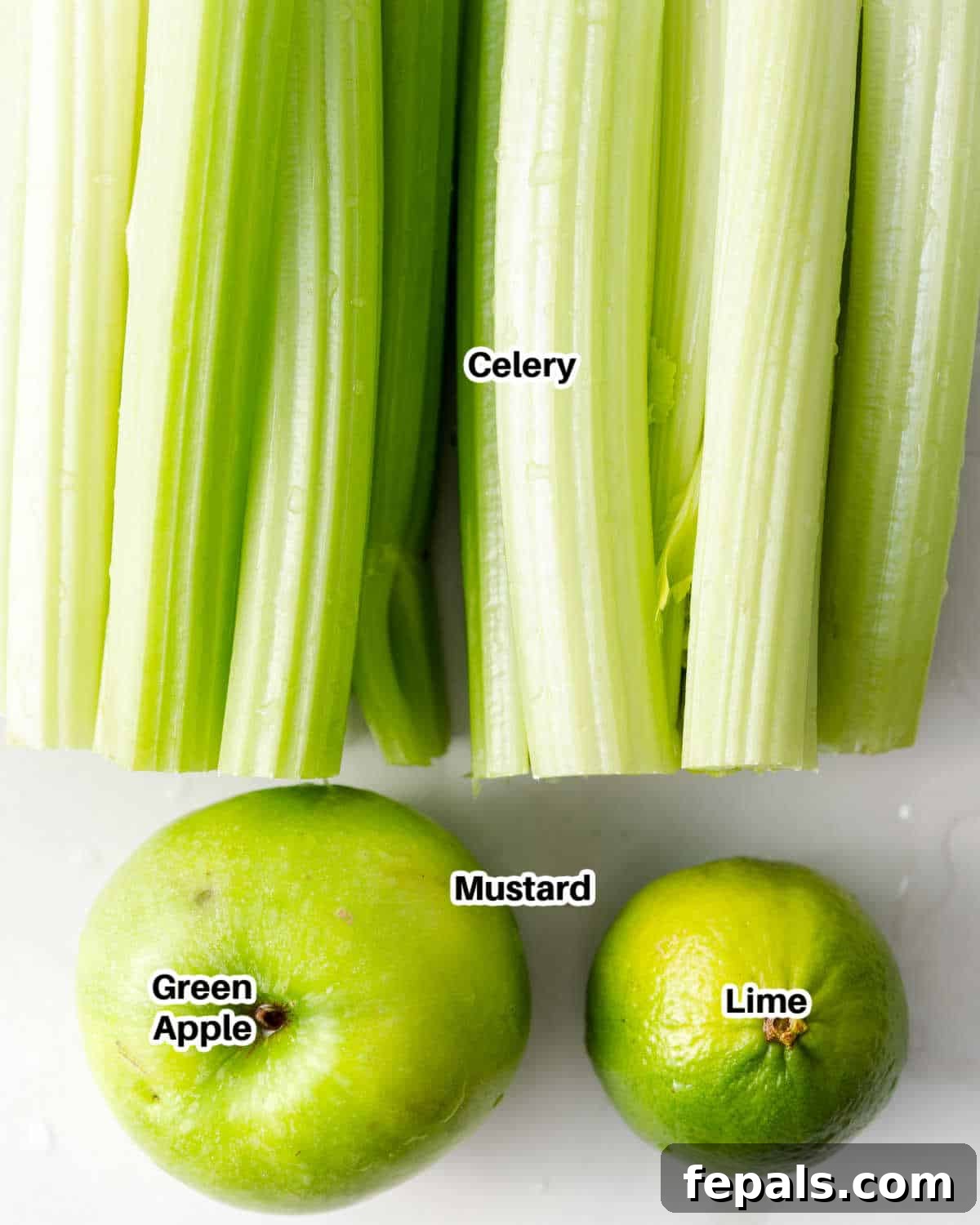 Fresh ingredients for celery juice: celery stalks, a green apple, and a lime on a wooden surface.