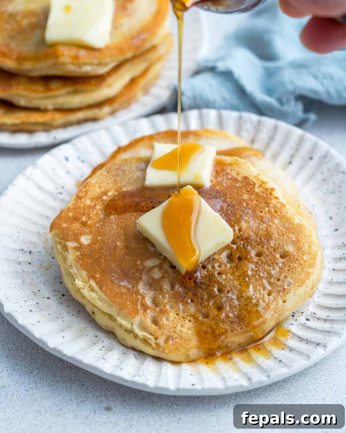 Make Pancake Mix from Scratch in 5 Minutes 7 Cooked pancakes on a white plate with pats of butter and a drizzle of maple syrup.